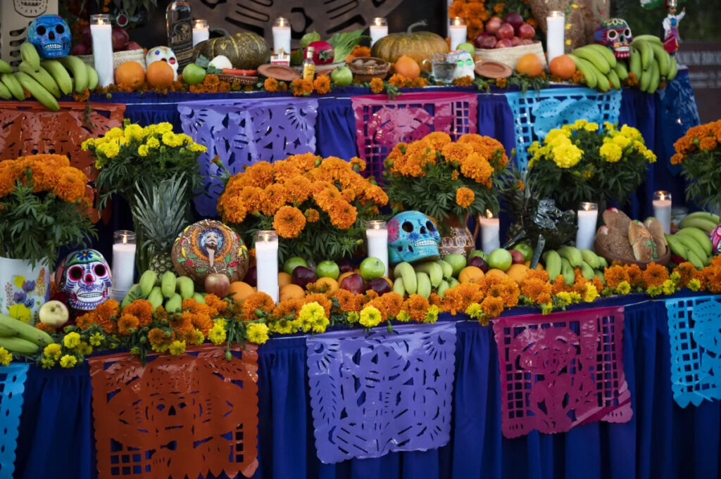Foto de um altar do Día de los Muertos. Há muitas flores, frutas, velas e caveiras de açúcar.