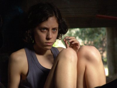 Imagem de Alex, protagonista do filme XXY. Nela, Alex está sentada em um espaço aparentemente apertado, de modo que seu cabelo curto e castanho se mistura levemente com o fundo. Ela usa uma regata acinzentada e carrega uma expressão frustrada, destacando seus olhos azuis claros.