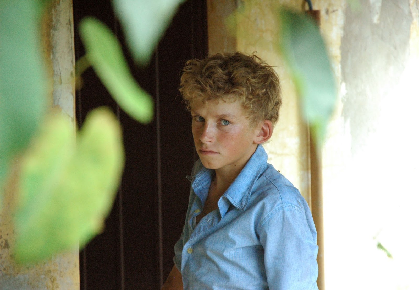 Foto de Mario, personagem do filme O Último Verão da Boyita. Mario pele clara, cabelos loiros curtos e encaracolados e olhos azuis, que se assemelham a camisa também azul que ele está vestindo